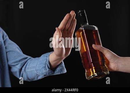 Alcoolisme. Homme refusant la bouteille de whisky sur fond noir, gros plan Banque D'Images