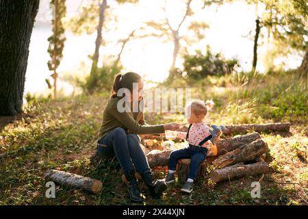 Maman nourrit une petite fille avec du porridge d'une cuillère assise sur des souches dans la forêt Banque D'Images