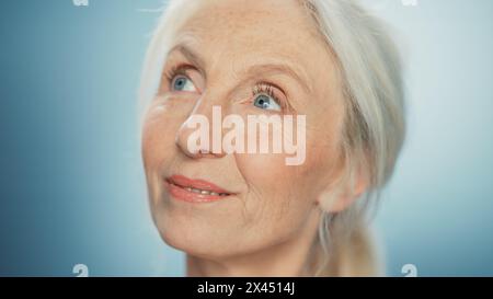 Gros plan Portrait de belle femme senior regardant loin merveilleusement. Magnifique grand-mère âgée regardant avec beauté naturelle des cheveux gris, yeux bleus et vision du monde joyeuse Banque D'Images