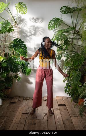 Positive fille noire dansant pieds nus sur plancher en bois dans des écouteurs écoutant de la musique profitez du moment. Banque D'Images