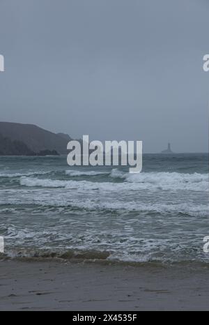 Paysages magnifiques en France, Bretagne. Plage de Baie des Trepasses à Plogoff. Surfeurs et vieux phare (Phare de la vieille). Jour de printemps nuageux. Se Banque D'Images