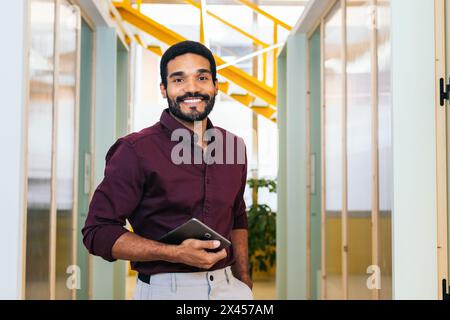 Portrait d'homme afro-américain souriant dans la chemise tenant la tablette dans le bureau moderne Banque D'Images