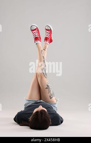 Femme avec de beaux tatouages couchés sur fond gris Banque D'Images