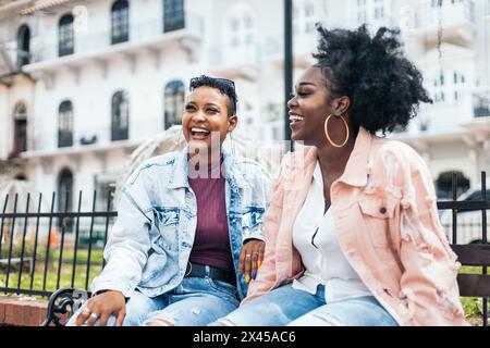 Deux amies noires parlant assis sur un banc riant et s'amusant dans la ville Banque D'Images