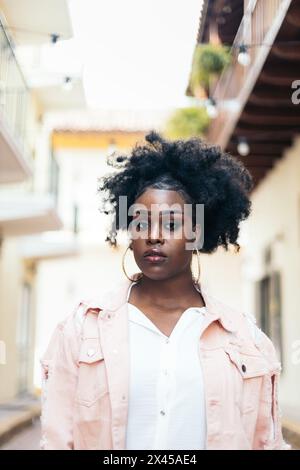 Portrait d'une jolie femme noire aux cheveux afro regardant la caméra. Elle a quelques caractéristiques et semble confiante. Banque D'Images