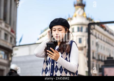 Jeune femme chinoise adulte dans des vêtements de mode à l'aide d'un smartphone dans les rues d'une ville européenne Banque D'Images