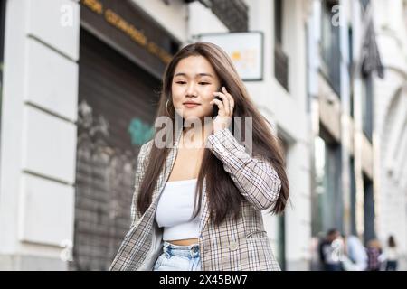 Jeune femme asiatique parlant au téléphone marchant dans les rues d'une ville européenne Banque D'Images