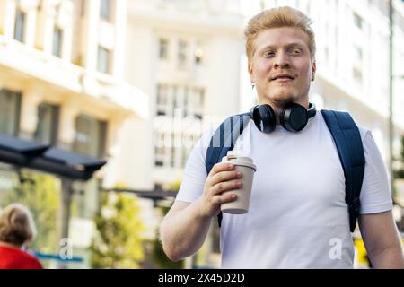 Jeune homme latino qui est albinos marchant dans la rue de la ville en écoutant de la musique avec des écouteurs un matin d'été. Il porte des vêtements blancs et un bleu Banque D'Images