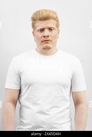 Gros plan portrait des traits du visage d'un albinos latino. Ses longs cils blancs protègent ses yeux bleus de la lumière du soleil. Il porte un caillot entièrement blanc Banque D'Images