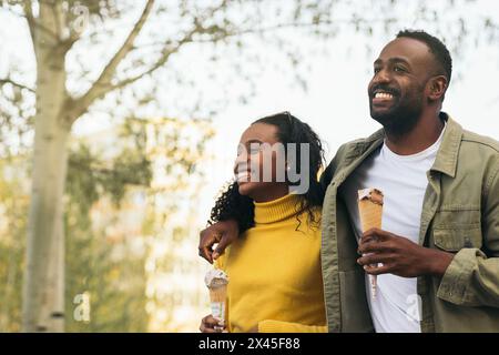 un couple de noirs qui mange de la crème glacée dans un parc Banque D'Images