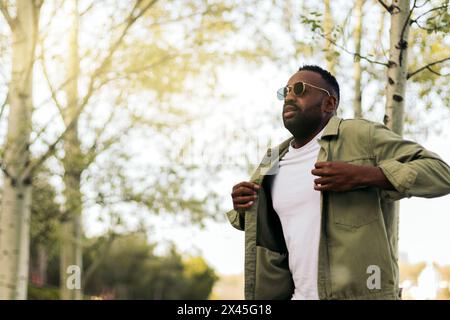 Jeune homme afro-américain élégant avec des lunettes de soleil marchant dans un stationnement Banque D'Images