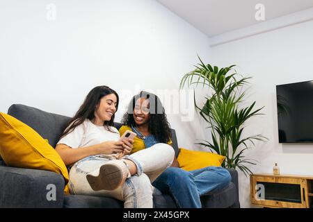 Connecté à la maison : deux jeunes femmes utilisant des appareils mobiles Banque D'Images