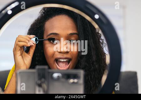 Jeune femme influenceuse réalisant un blog vidéo de maquillage pour les médias sociaux. Il est enregistré avec un smartphone et avec un anneau lumineux à la maison. Concept de beauté Banque D'Images
