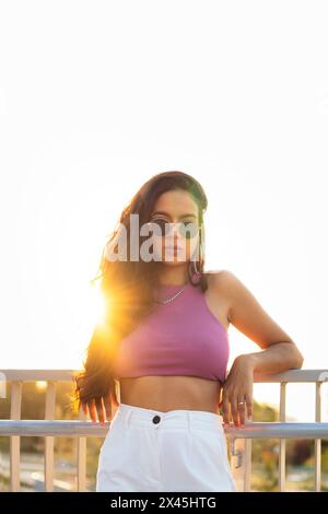 Portrait au coucher du soleil d'une jeune femme latina avec des lunettes de soleil regardant la caméra et posant Banque D'Images