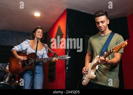 groupe de musiciens répétant leurs chansons dans une salle d'enregistrement et de répétition musicale. Une fille chante et joue de la guitare, un garçon joue de la guitare électrique Banque D'Images