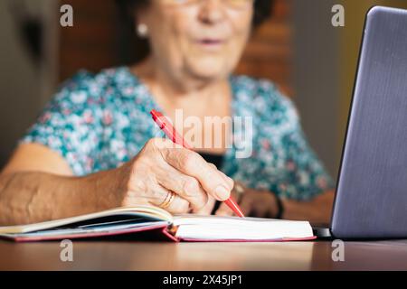 Gros plan d'une vieille femme écrivant dans un ordinateur portable tout en utilisant son ordinateur portable à la maison. Banque D'Images