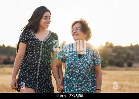 Femme âgée souriante dans un beau champ de tournesols au coucher du soleil avec sa petite-fille profitant du temps ensemble Banque D'Images