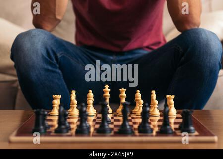 La partie d'échecs est sur le point de commencer. Homme méconnaissable assis sur un canapé devant un échiquier avec les pièces placées. Banque D'Images