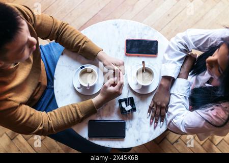 Plan aérien d'une table de cafétéria où deux personnes boivent du café. Un homme asiatique et une femme latino-américaine ont rendez-vous dans un café et parlent calmement. Banque D'Images