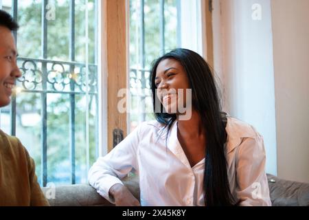 Portrait d'une femme latina souriante parlant à un homme asiatique. Le lieu de rencontre est à l'intérieur et la lumière est chaude Banque D'Images