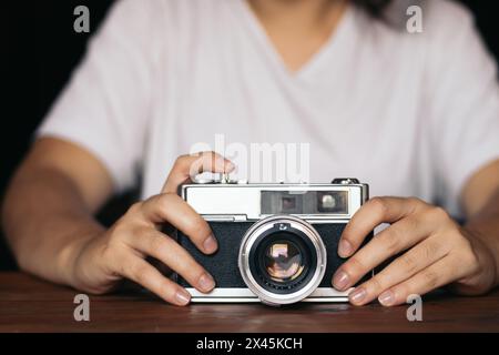 Gros plan d'une caméra analogique sur une table en bois. Une personne méconnaissable la tient. Banque D'Images