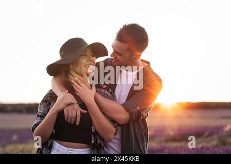 Belle photographie en contre-jour d'un jeune couple aimant se promenant dans un champ de lavande au coucher du soleil. Banque D'Images