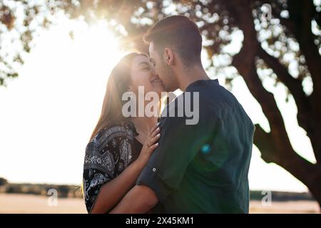 Jeune couple profitant d'une belle et ensoleillée journée à la campagne. Ils s'embrassent et s'embrassent, heureux d'être ensemble Banque D'Images