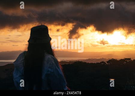 Femme méconnaissable regardant un beau coucher de soleil dans la campagne au Costa Rica. Le soleil se couche sur les montagnes Banque D'Images