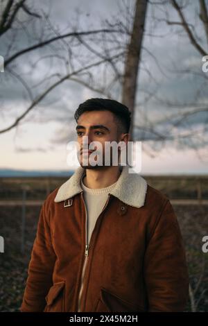 Portrait d'un jeune homme attrayant regardant loin dans une veste brune à l'extérieur dans la nature Banque D'Images