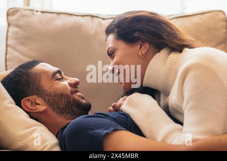 Moment romantique entre un jeune homme et une jeune femme assis ensemble sur un canapé confortable dans leur maison. Banque D'Images