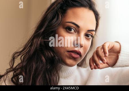Portrait d'une jeune femme magnifique près d'une fenêtre. La femme regarde par la fenêtre. Parfait pour le style de vie, la beauté ou les projets sur le thème de la relaxation. Banque D'Images