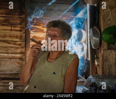 Une femme cultivatrice de café dans la ferme fumant un cigare tout en préparant du café sur un café à feu ouvert, près de Vinales, Cuba Banque D'Images