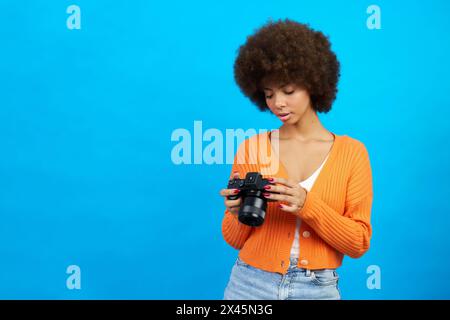 une photographe aux cheveux afro avec un appareil photo dans les mains qui passe en revue les photos qu'elle a prises Banque D'Images