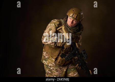 Portrait d'un jeune homme équipé comme un militaire posant avec un fusil automatique airsoft avec viseur télescopique Banque D'Images