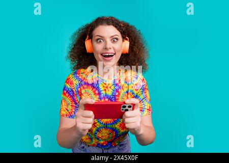 Photo de la femme joyeuse heureuse porter des vêtements imprimés élégants ont un jeu de jeu amusant isolé sur fond de couleur cyan Banque D'Images