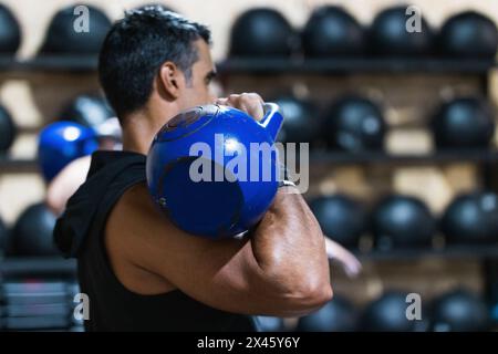 Vue latérale d'un sportif hispanique musclé qui pèse un poids lourd lors d'une séance d'haltérophilie en salle de sport avec équipement sportif Banque D'Images