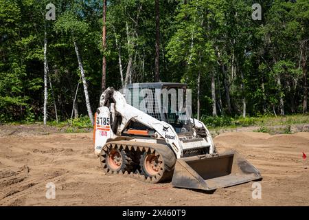 CROW WING CO, MN - 6 juin 2021 : une Bobcat S185, chargeuse frontale compacte blanche, avec chenilles de direction à glissement, est assise sur la terre dans un terrain de construction vide bordé d'arbres, Banque D'Images