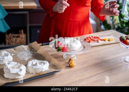 Deux chefs dans une cuisine dynamique collaborent à décorer un pavlova avec des fraises fraîches et de la crème, mettant en valeur leurs compétences culinaires et leur travail d'équipe. H Banque D'Images