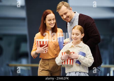 Un homme et sa famille tiennent joyeusement des boîtes de pop-corn au cinéma, se liant tout en regardant un film ensemble. Banque D'Images