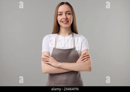 Belle jeune femme portant tablier de cuisine sur fond gris. Maquette pour le design Banque D'Images