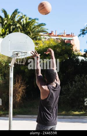 Vue arrière d'un athlète afro-américain méconnu jouant au basket-ball sur le terrain en été et en regardant la caméra Banque D'Images