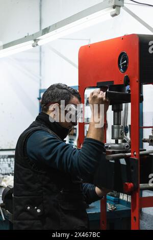 Vue latérale d'un mécanicien automobile masculin dans des lunettes de protection à l'aide de presse hydraulique lors de l'installation des roulements des véhicules Banque D'Images