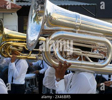 Gros plan d'un tuba en laiton poli avec les mains d'un musicien, des membres du groupe en chevalet blanc en arrière-plan, lors d'un défilé urbain à Cancun, au Mexique Banque D'Images