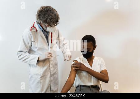 Homme médical faisant l'injection pour la patiente noire dans le masque Banque D'Images