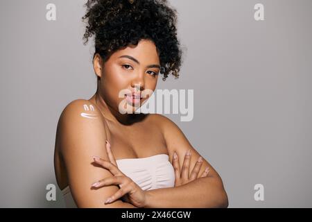 Femme afro-américaine aux cheveux bouclés, debout dans un studio, les bras croisés enveloppés dans une serviette blanche. Banque D'Images