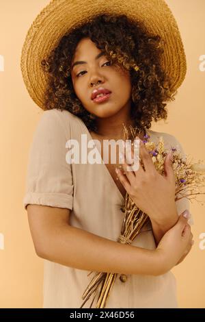 Une belle jeune femme afro-américaine aux cheveux bouclés portant un chapeau de paille, tenant un bouquet de fleurs colorées. Banque D'Images