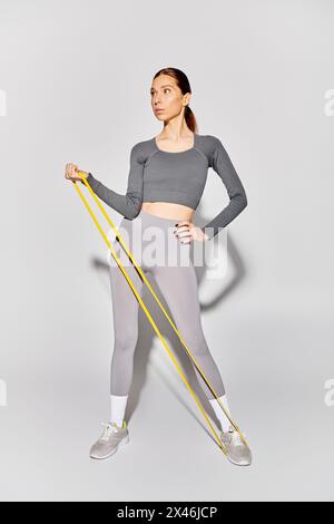 Une jeune femme sportive en vêtements actifs travaillant avec des élastiques sur un fond gris. Banque D'Images