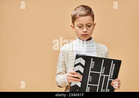 Un garçon préadolescent mignon habillé en réalisateur tenant un tableau noir et blanc de clap. Banque D'Images