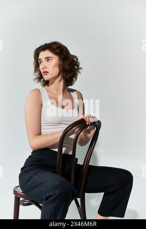 Une jolie jeune femme pose gracieusement sur une chaise en bois, dégageant élégance et confiance dans un cadre de studio. Banque D'Images