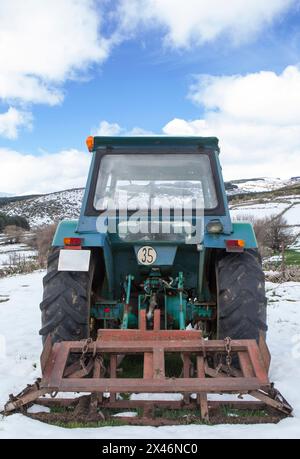 Vieux tracteur équipé d'un outil stationné au milieu d'une prairie enneigée. Concept d'agriculture de montagne Banque D'Images